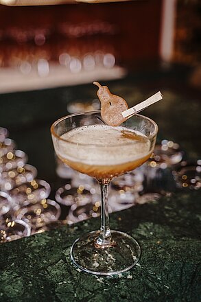 Elegant cocktail in coupe glass garnished with dried pear on a dark green marble bar