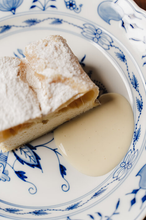 Apple strudel dusted with powdered sugar served with vanilla sauce on porcelain plate
