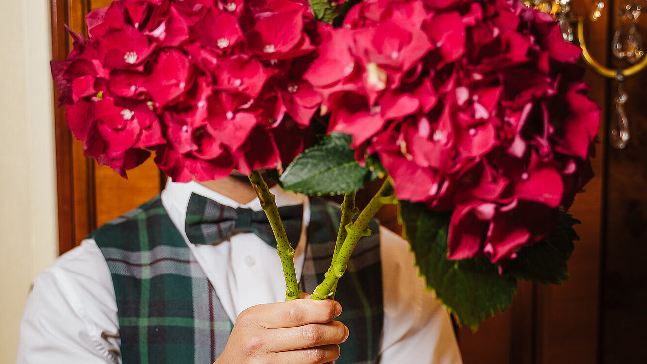 Man in formal vest holding large bouquet of red hydrangeas indoors