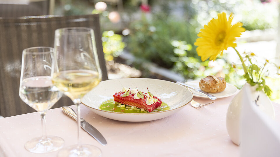 Gourmet salmon tartare with garnish served outdoors with white wine and a flower vase