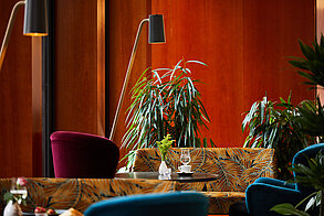 Cozy café interior with patterned seating, indoor plants and warm wooden panel walls