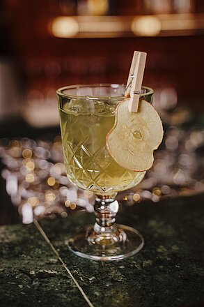 Green cocktail in cut glass with ice and dried apple slice garnish on marble bar